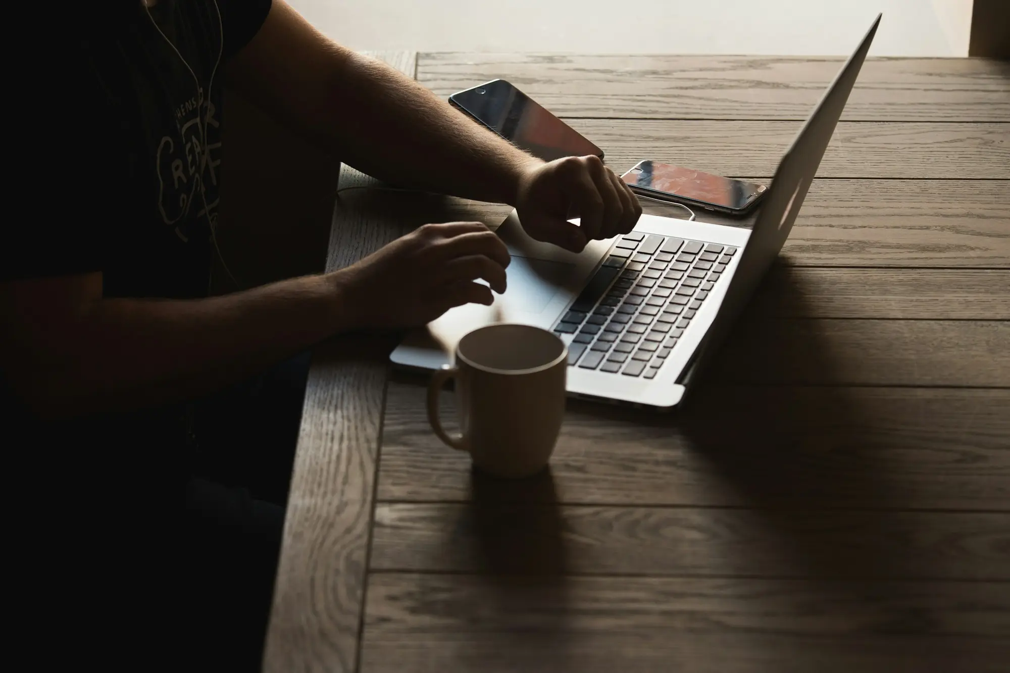 Manos escribiendo en un portátil, con una taza de café sobre la mesa
